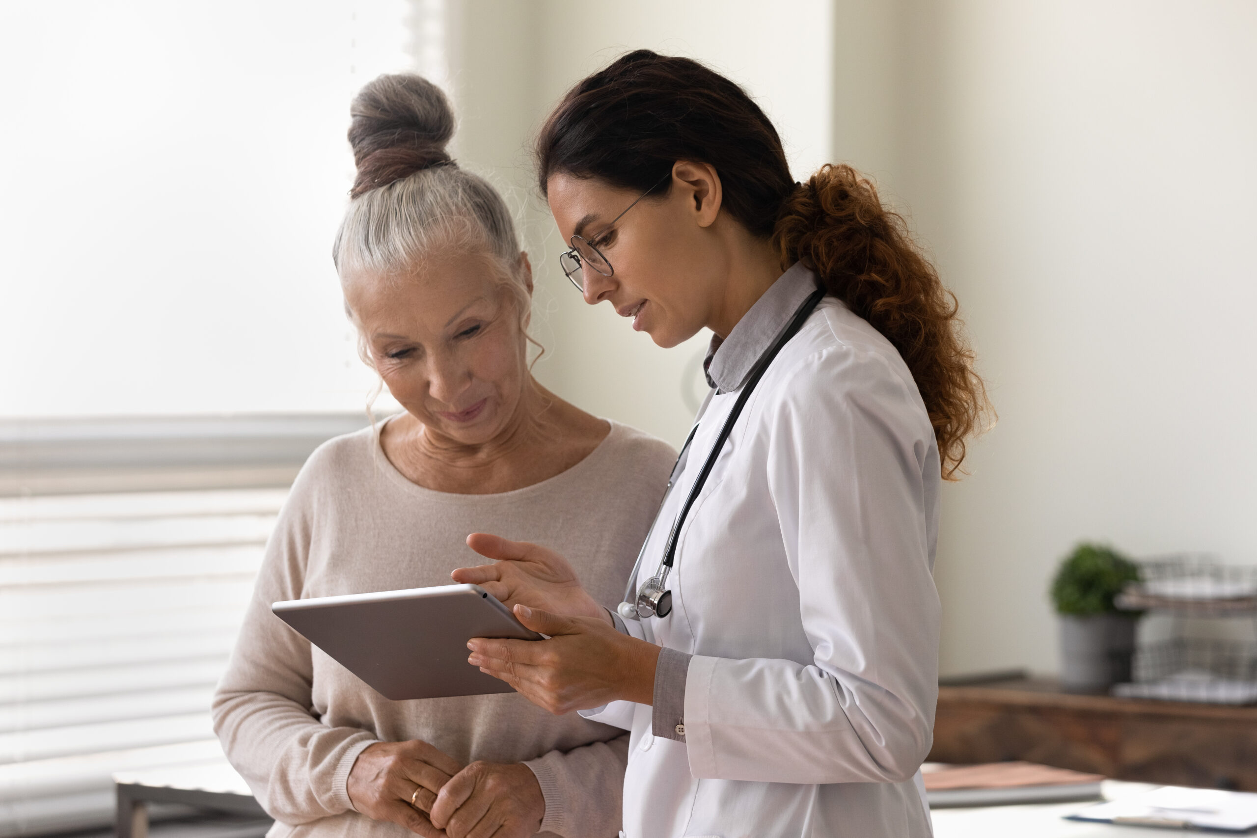 Serious GP doctor showing tablet screen to old female patient